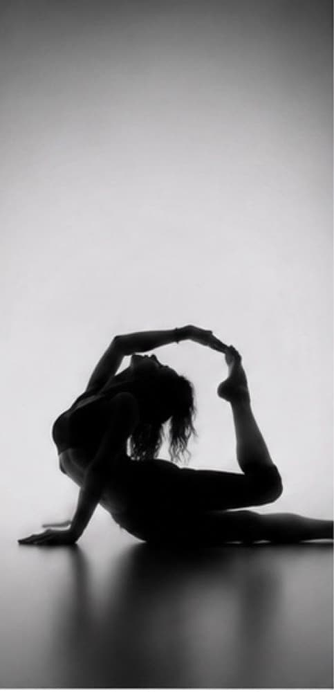 Silhouette of a dancer on the floor, her hands reaching her raised foot