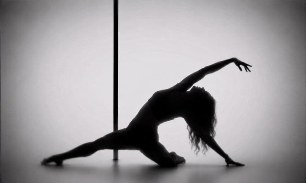 Silhouette d’une danseuse au sol devant la barre, un bras tendu