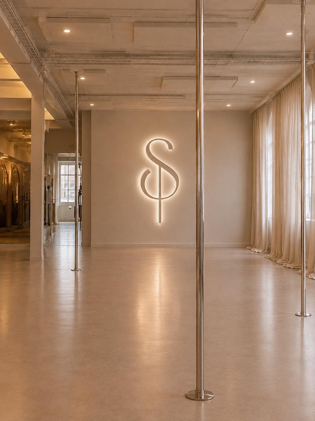 Projection du studio : la salle vue vers le mur au monogramme lumineux, barres chromées, rideaux clairs et sol beige dans la lumière du soir.